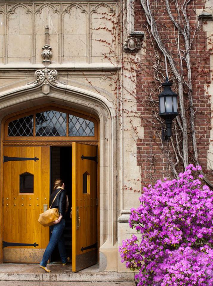 Female students walks through wooden doors of building on SUNY Geneseo campus
