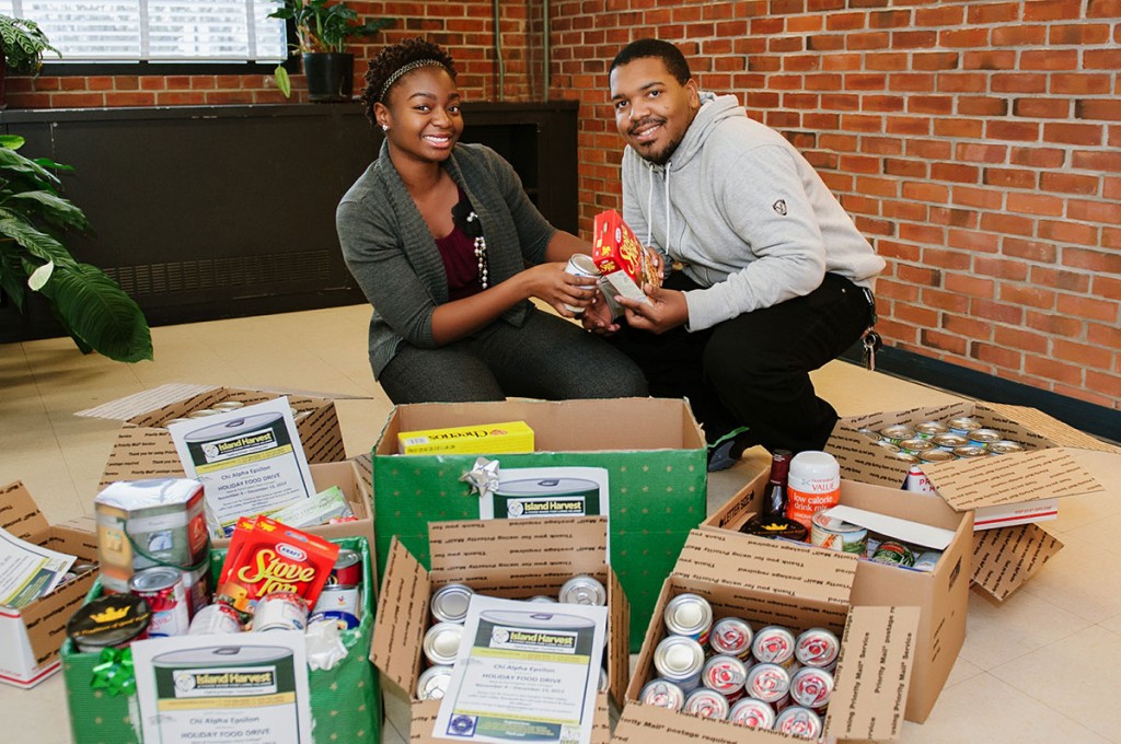 Farmingdale State College students kneel behind boxes of donated food stuffs