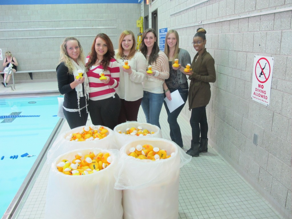     Genesee Community College students stand pool-side with buckets of rubber ducks at the campus Ducky Derby