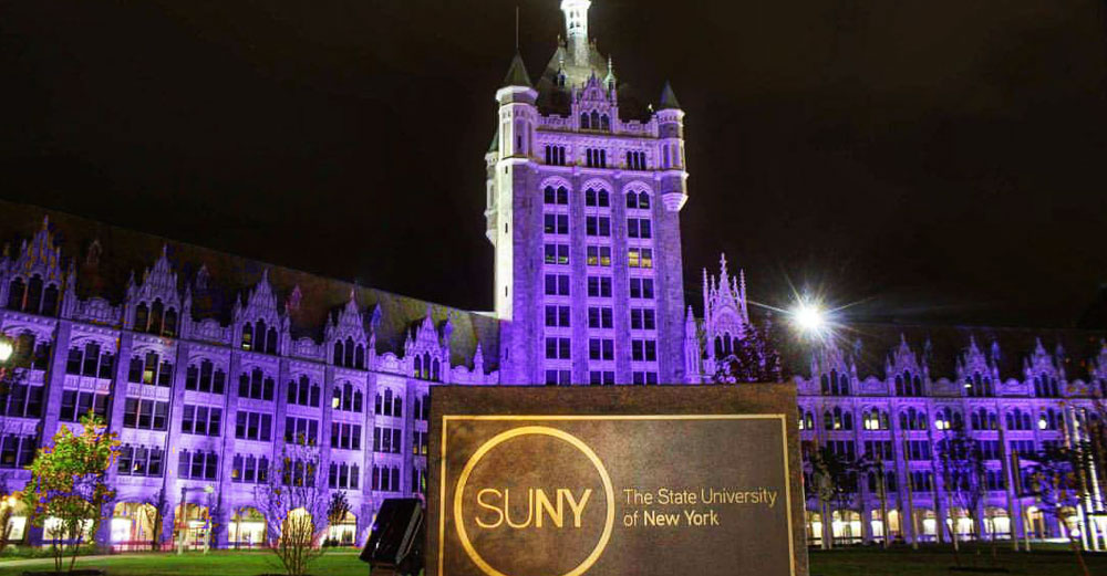 SUNY Plaza at night shining in purple light with SUNY sign in front.