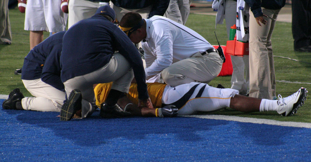 Football player down on the field with medical staff looking him over. 