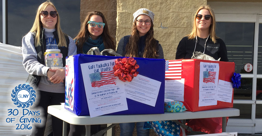 Female students at Fredonia stand behind table collecting care package <a href=