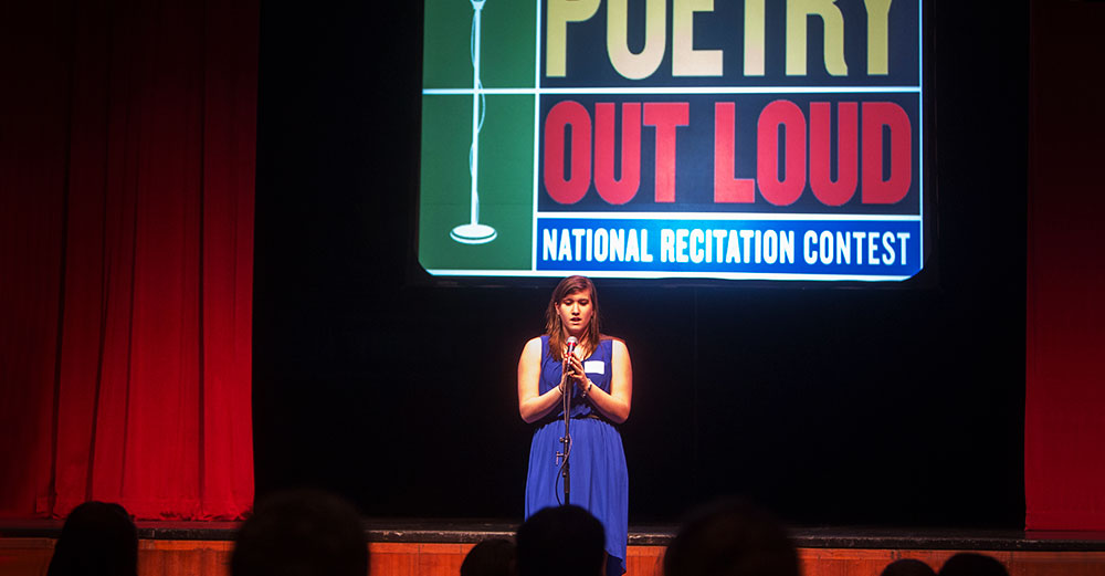 A student stands on stage at a Poetry Out Loud competition at Binghamton University