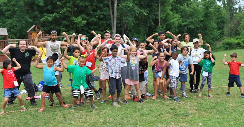 Stony Brook students with children at Camp Kesem pose for picture while flexing muscles outside at camp.