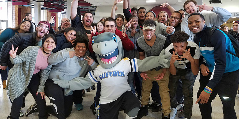 Finn Shark from SUNY Suffolk County Community College kneeling with a bunch of students raising their hands. 