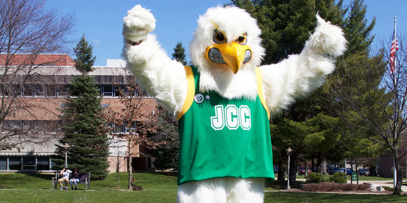 Jamestown Community College mascot JJ stands outside with arms raised. 