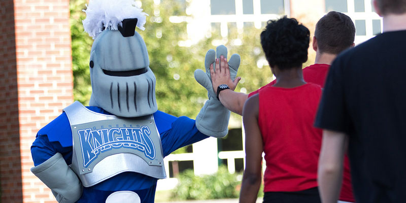 Geneseo Knight giving high fives to students outside.