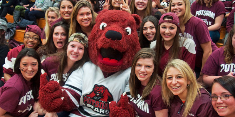 Potsdam mascot Max C bear sits in the stands with student fans. 
