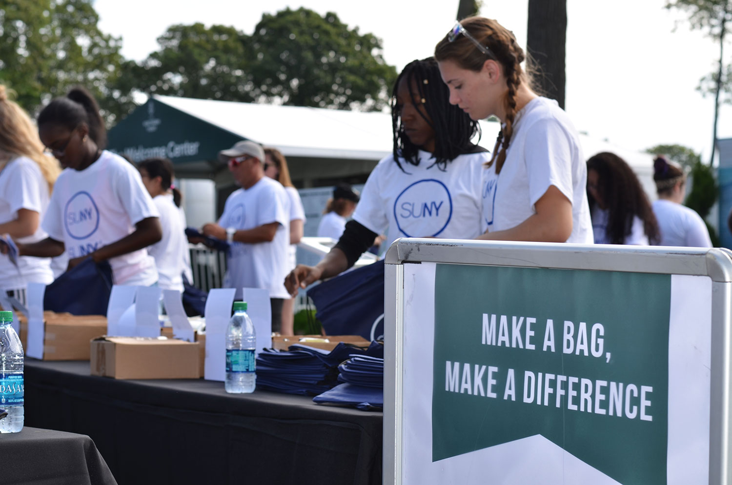 Student volunteers fill comfort bags at the Northern Trust Open in Old Westbury in front of a sign that says Make A Bag, Make A Difference.