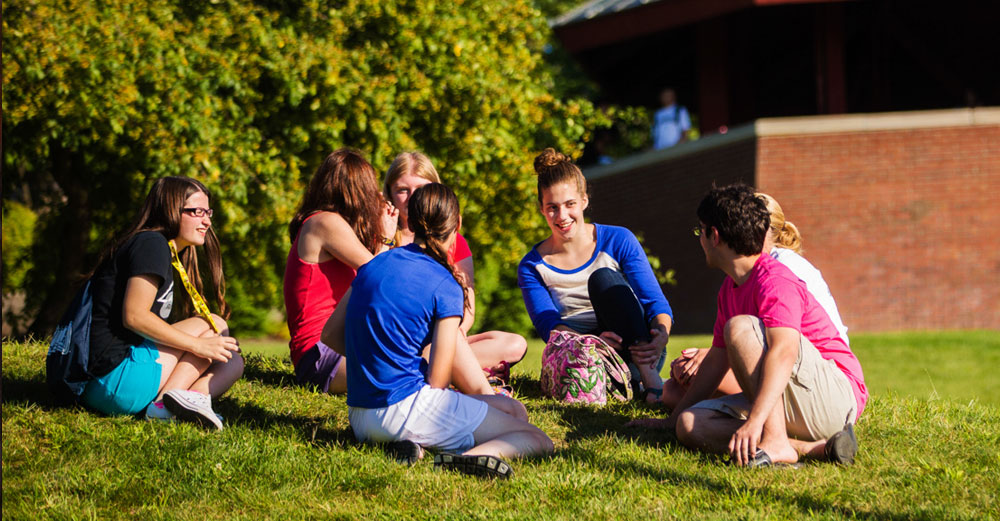 Students at SUNY Geneseo sit and talk on the lawn during a bright sunny day.