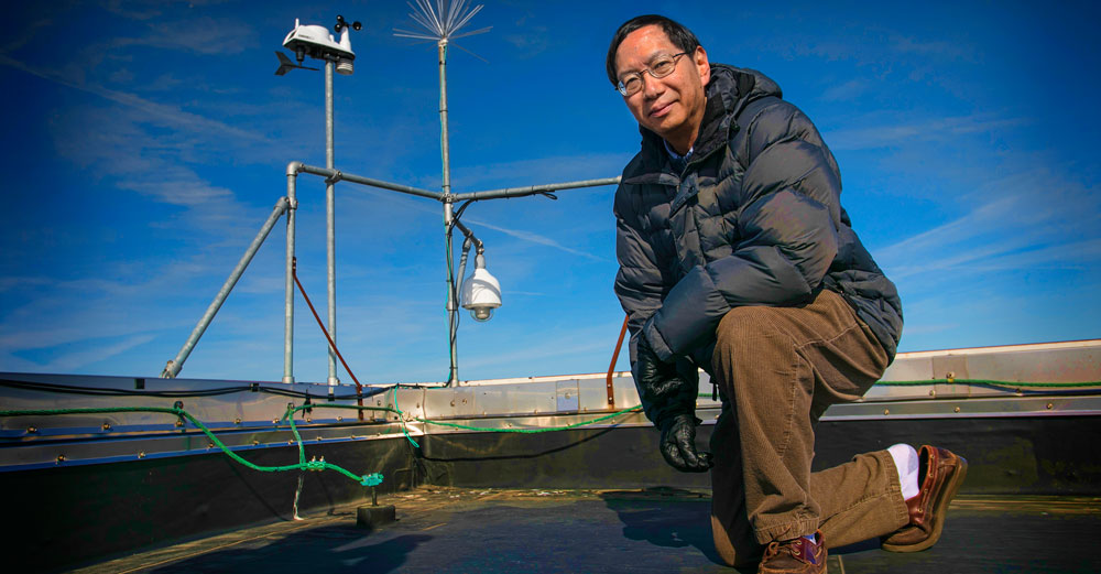 Dr Edmund Chang of Stony Brook University kneels on a rooftop in front of weather measuring tools. 