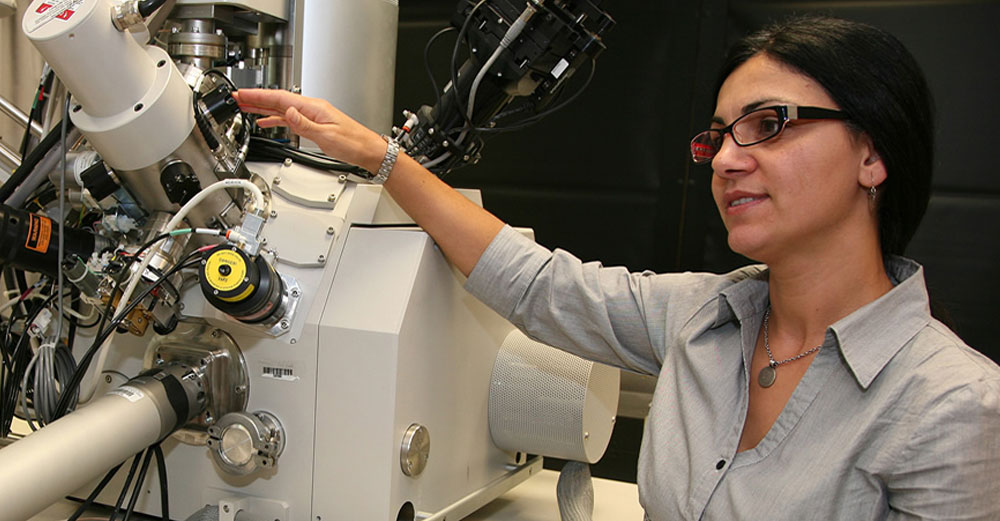 A female researcher stands in the lab near a scientific magnification tool.