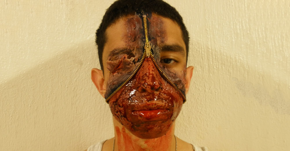 Student with bloody face makeup and a latex zipper opening into his face.