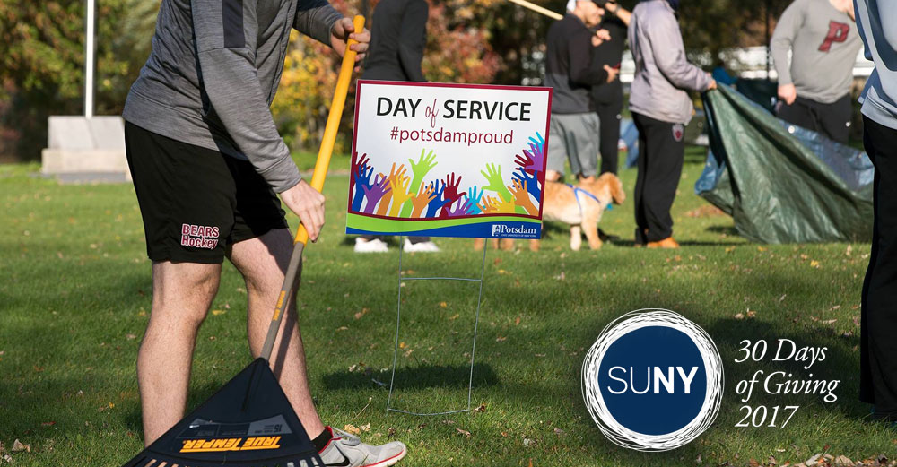 A SUNY Potsdam student rakes leaves in front of a sign saying Day of Service #PotsdamProud.