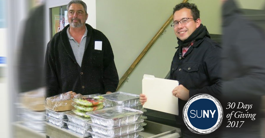 A male student and male staff member from Mohawk Valley Community College stand behind prepared meal packages ready to donate to food banks.