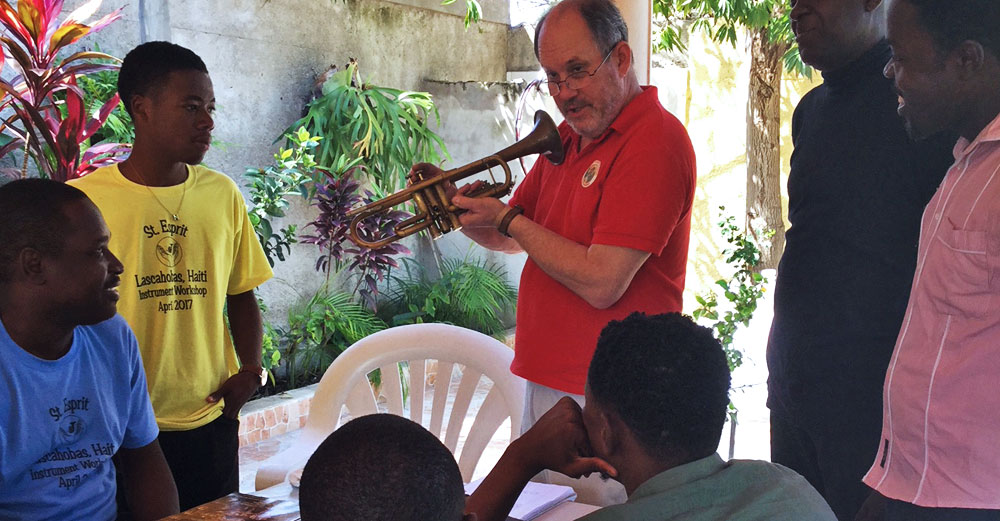 Bill Cole holds up a woodwind horn as he teaches locals in Haiti about it.