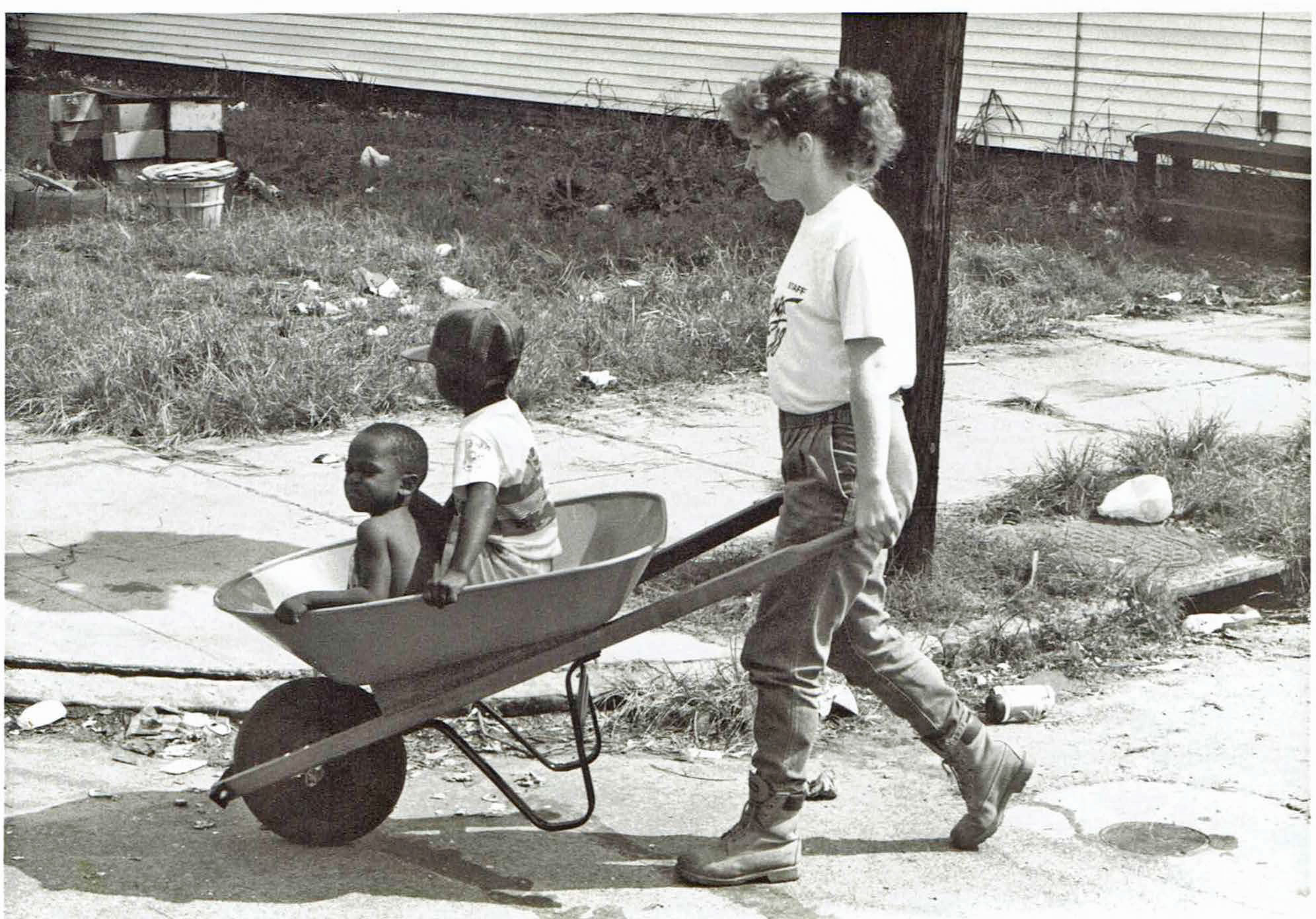 In 1989, a female SUNY Delhi volunteer pushes children to saefty in a wheelbarrow in hurricane damagaed Charleston, South Carolina.