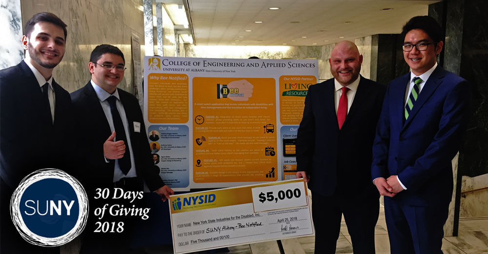 4 UAlbany College of Engineering and Applied Sciences students in suits stand in front of sign showcasing their BEE-notified project.