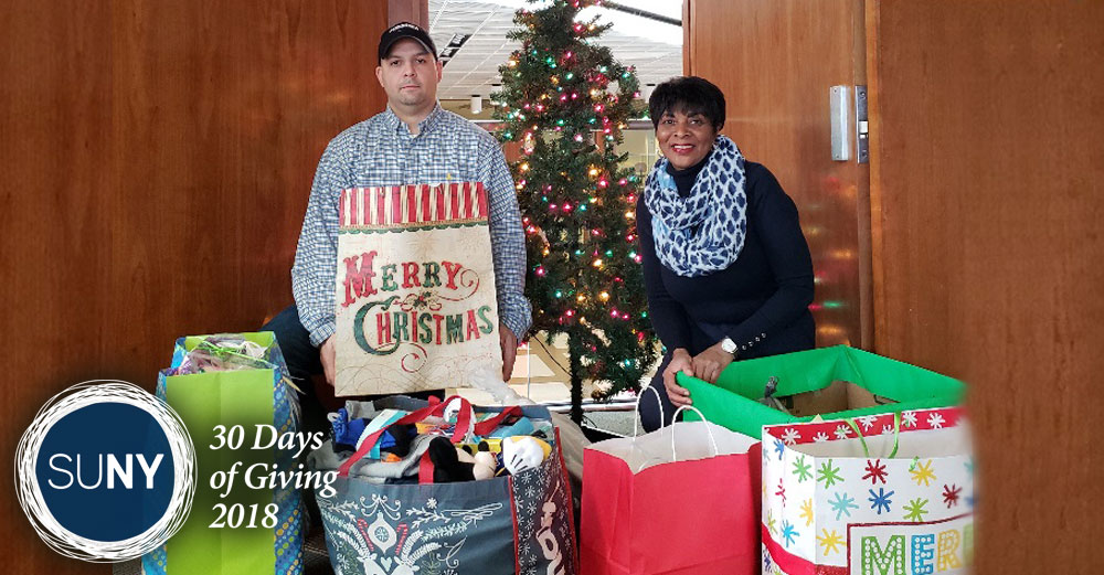 Two SUNY Fredonia staffers stand behind bags full of Christmas gifts.