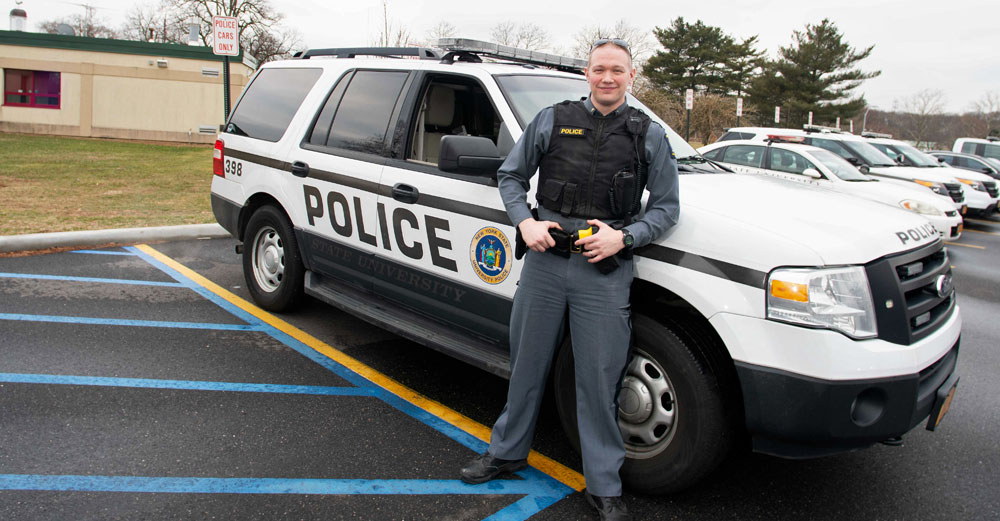 Lt. Zachary Lee of the Farmingdale State College University Police stands against his squad SUV outside. 
