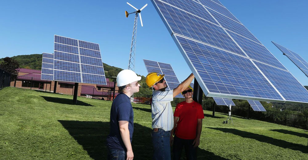 Students and teacher examine a large solar panel in the ground at SUNY delhi.