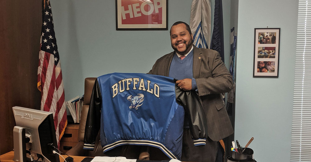 NYS Assemblyman Victor Pichardo in his office holding up his old UBuffalo jacket.