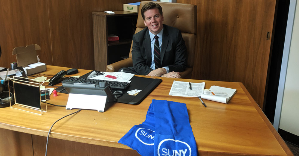 New York State Assemblyman Robert Carroll sits in his office with a SUNY scarf draped on his desk.