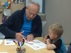 A toddler colors with an elderly man.