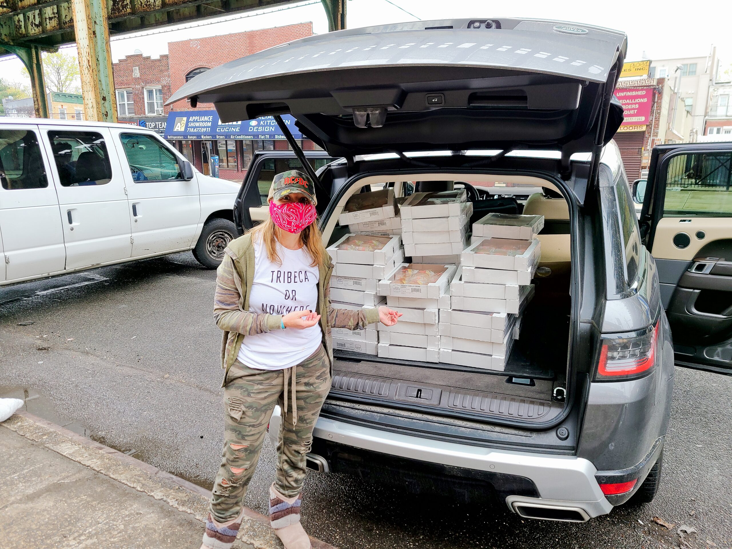 A woman stands near an SUV packed with boxes for a Food For The Frontline drop-off event.