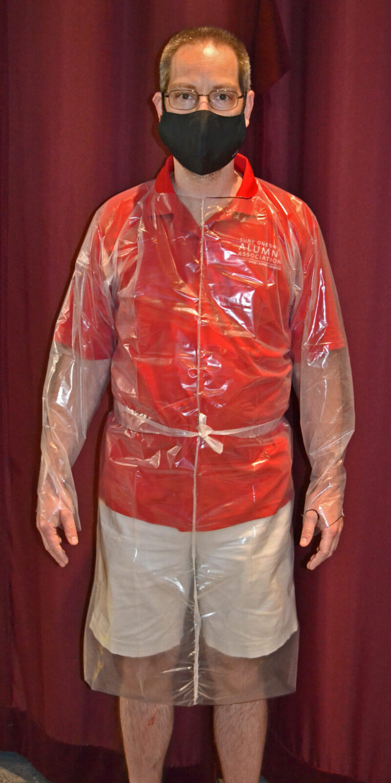 A man stands draped in a clear PPE hospital gown made by volunteers.