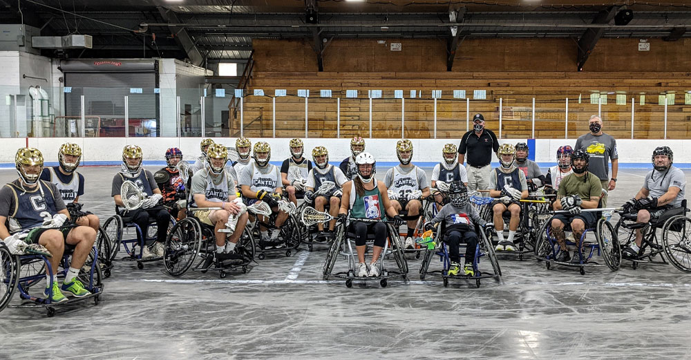 Members of the SUNY Canton lacrosse team pose with wounded military veterans in wheelchairs after playing wheelchair lacrosse in the arena.