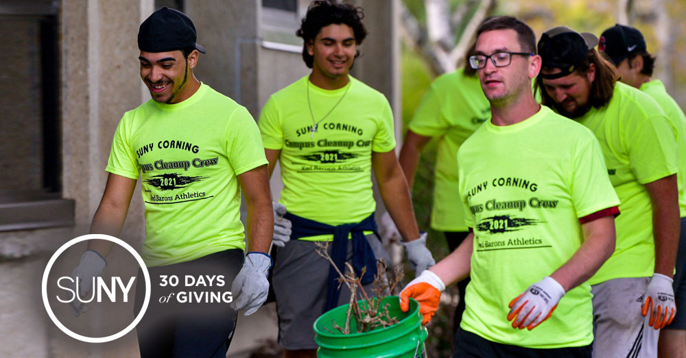 Students clean broken branches and debris outside while wearing SUNY Corning Community Cleanup Crew tshirts.
