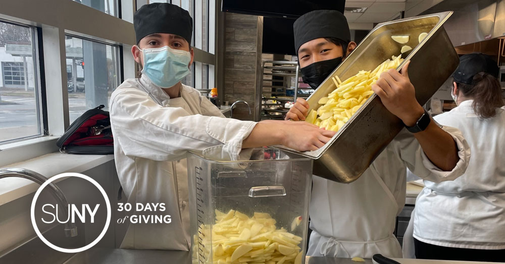 Culinary students in chef's coats and face masks dump sliced apples from tray into plastic container.