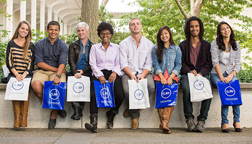 SUNY students sitting on wall with SUNY bags