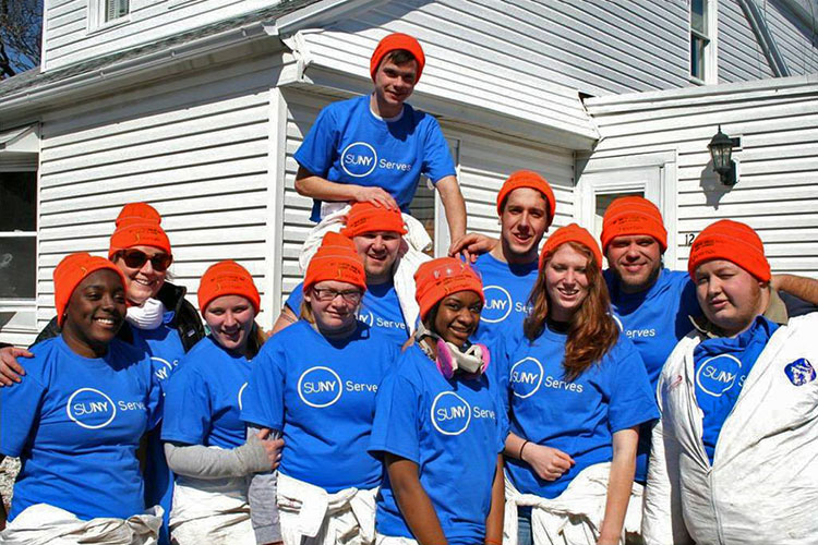 SUNY student volunteers wearing blue SUNY Serves t-shirts in front of a white house