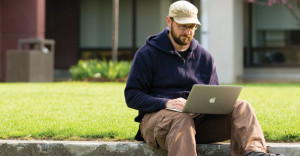 Student outside sitting on the grass with a laptop at Finger Lakes Community College