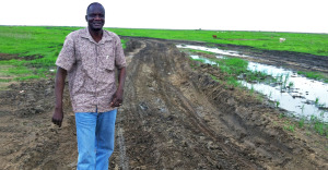 John Dau stands in a field on a muddy dirt road, smiling