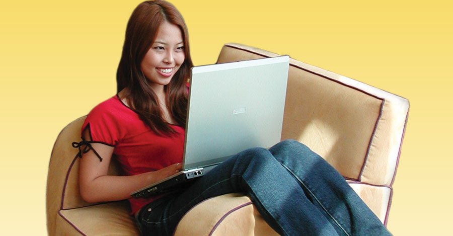 Asian girl sitting across easy chair working on laptop