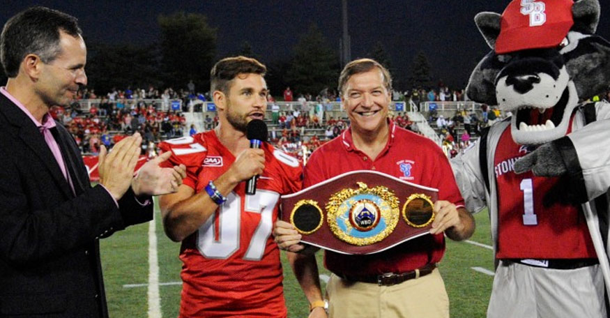 Chris Algieri stands in the middle of Stony Brook football field with his boxing championship belt and Wolfie Seawolf and President Stanley