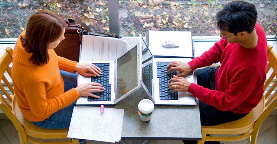 2 students at table on laptops facing each other