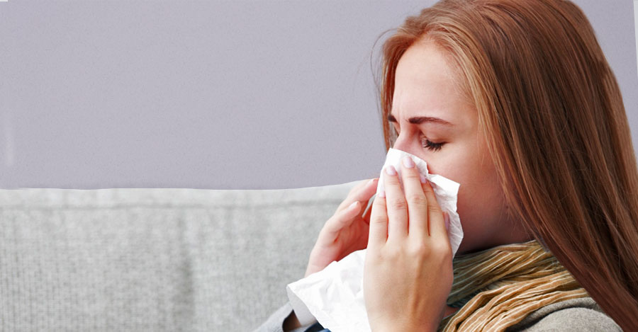 Sick girl blows her nose into tissue on couch. 