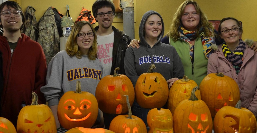 SUNY students behind Halloween carved pumpkin.