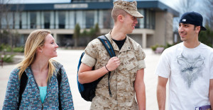 One student in military uniform and two students in casual clothes walk on college campus.