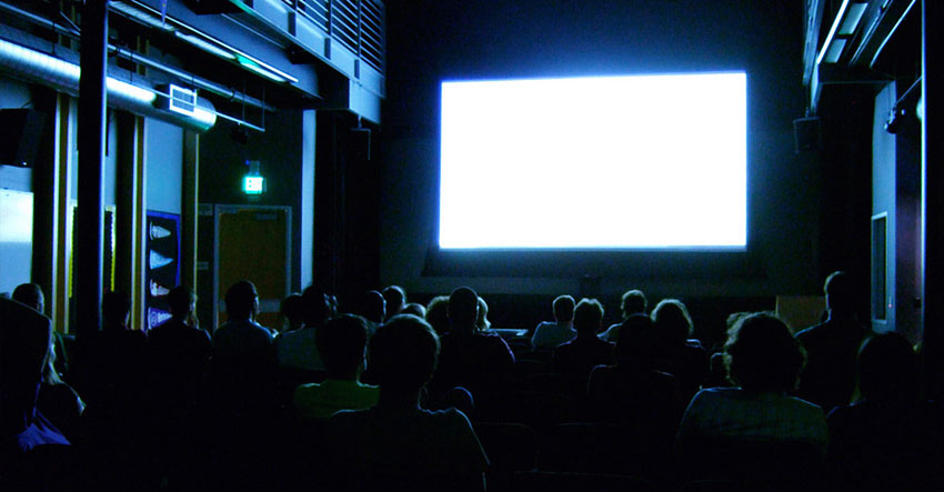 People in movie theater watching blank movie screen.