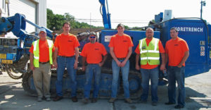 Farmingdale State College alum Arthur Corwin stands with his construciton crew outside in front of excavator.
