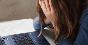 Student with face in hands sitting at laptop.