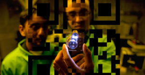 2 UAlbany researchers hold a light up to a drug container with a QR code superimposed over it.
