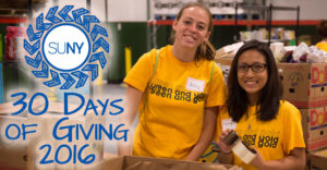 2 female students in front of boxes during a food drive. SUNY 2016 30 Days of Giving