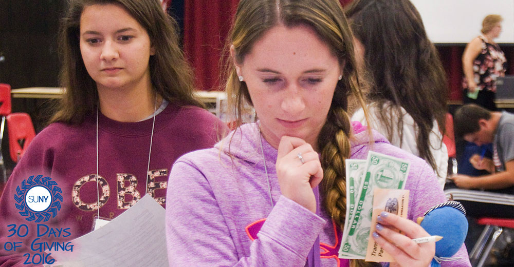 Sarah Prentice, a SUNY Cortland sophomore, clutches her “baby” Clarice as she purchases food during a poverty simulation at the college on. In line behind her is Alexandra Cicero, also a sophomore.