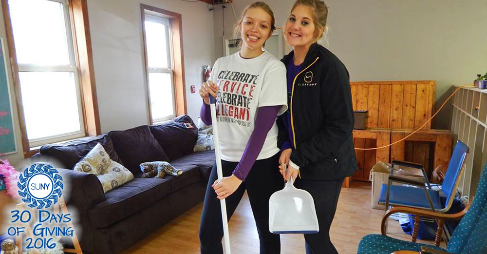 2 female Alfred State students with brooms in hand inside a house doing clean up.